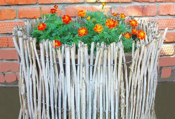 decoración de los lados del macizo de flores con ramas delgadas, insertadas verticalmente en el marco de alambre